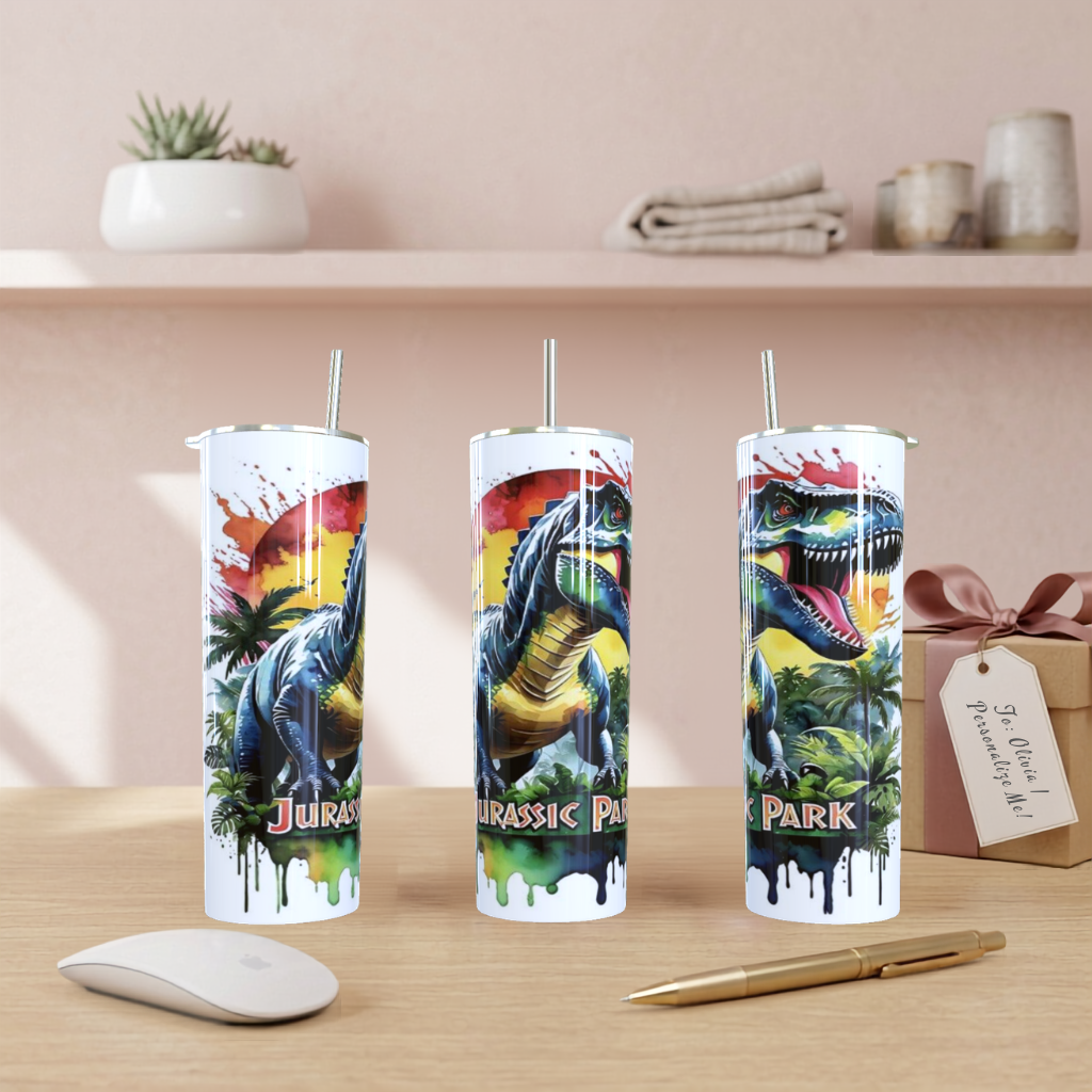 Three tall insulated tumblers with straws featuring colorful Jurassic Park dinosaur artwork, displayed on a wooden table with a mouse, pen, and gift box in a styled indoor setting.